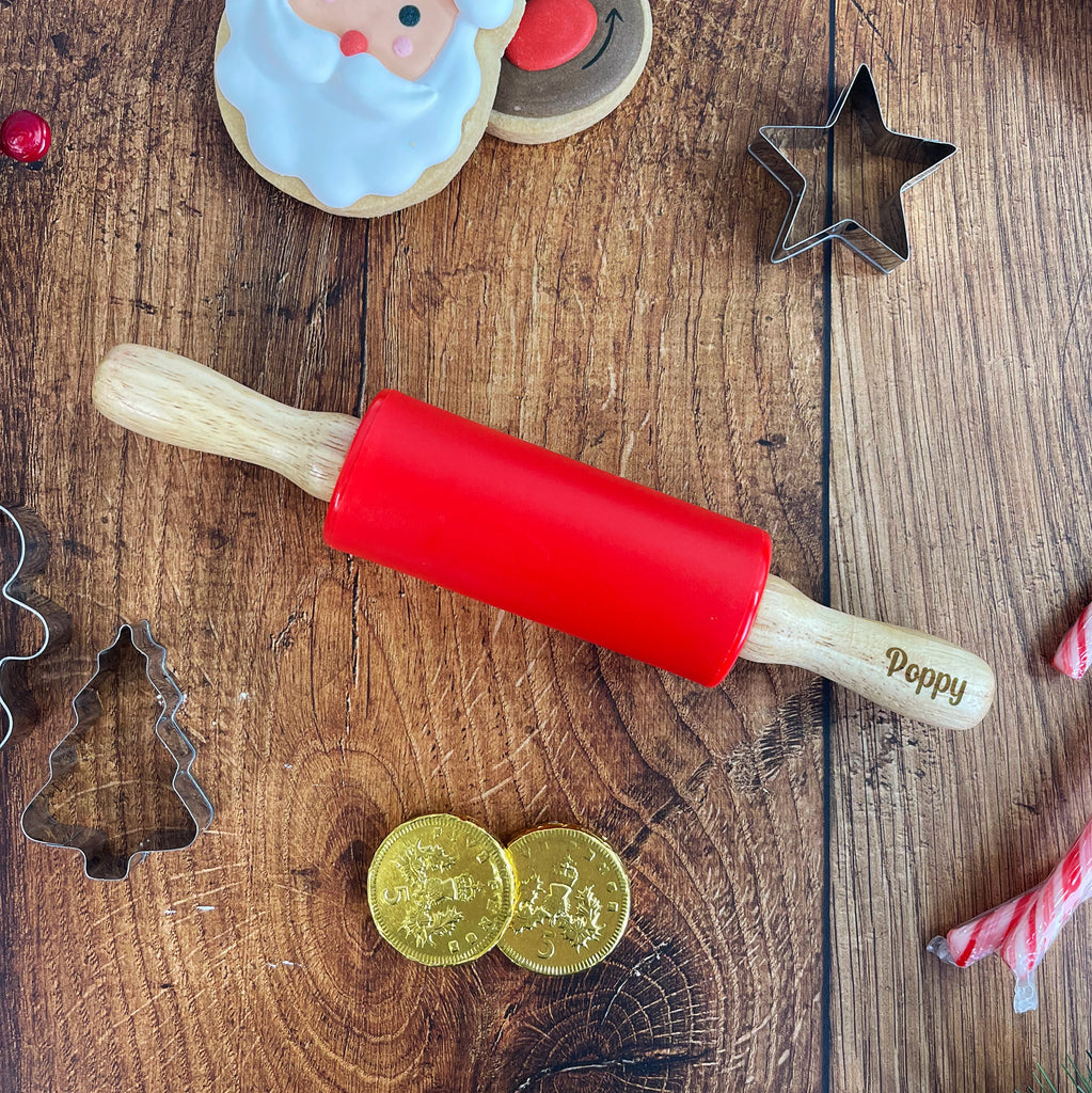 Red rolling pin with wooden handle on a wooden surface with Christmas-themed items.