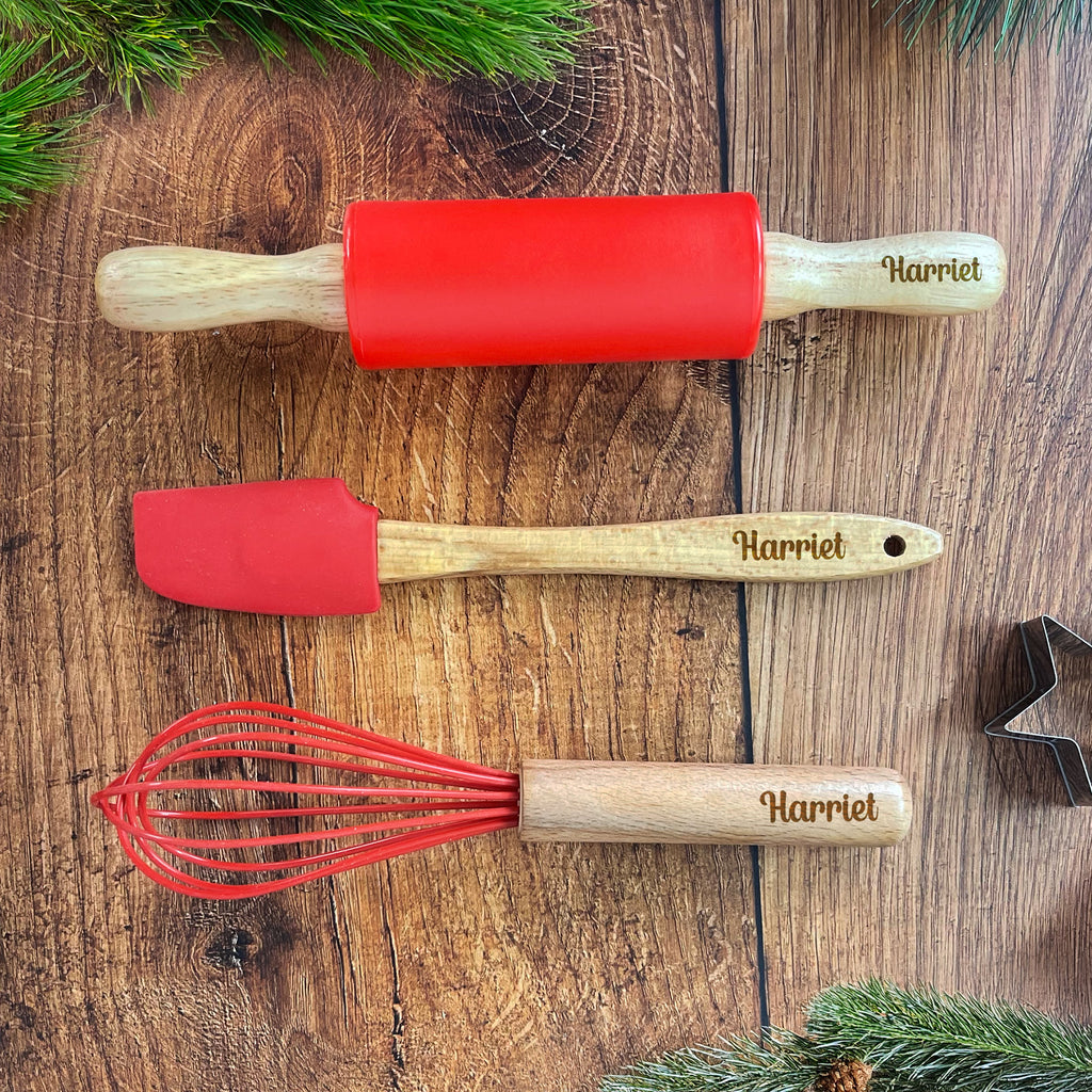 Three kitchen utensils with red silicone heads and wooden handles on a wooden surface.