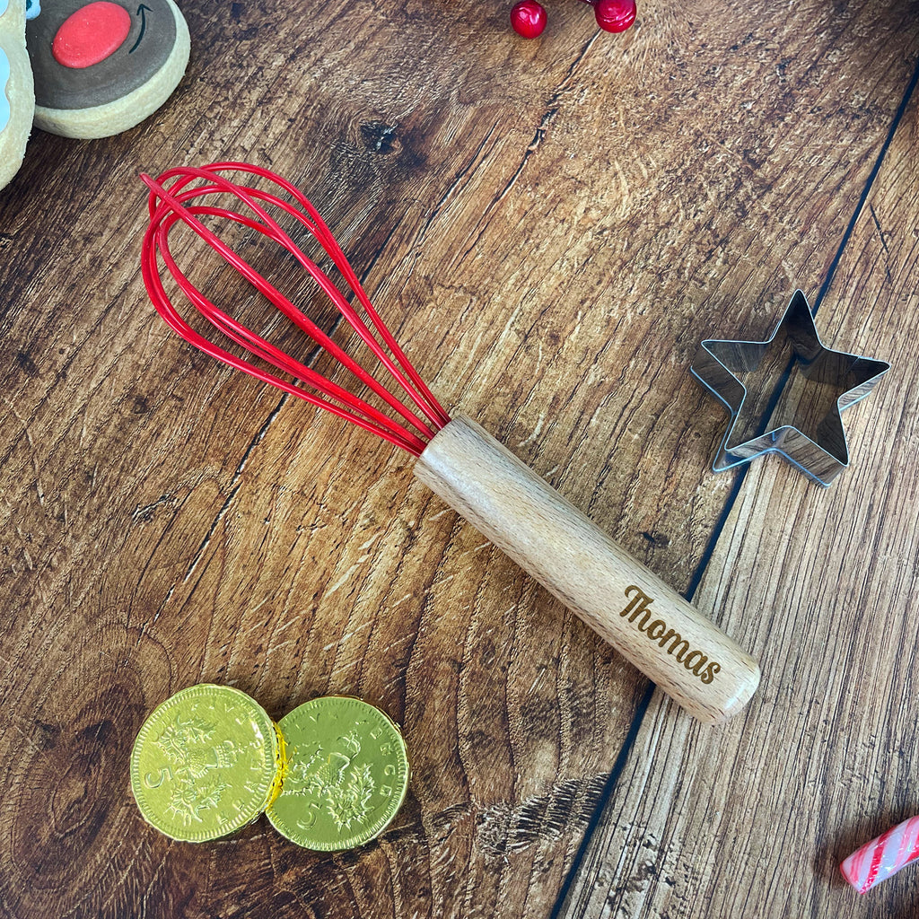 Wooden whisk with red whisk attachment on a wooden surface with cookies and cookie cutters.