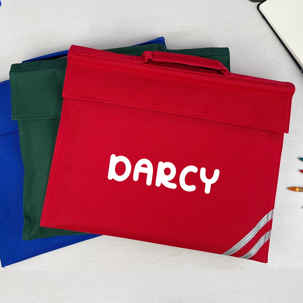 Red bag with 'Darcy' printed on it, surrounded by colorful folders and stationery items on a light surface.